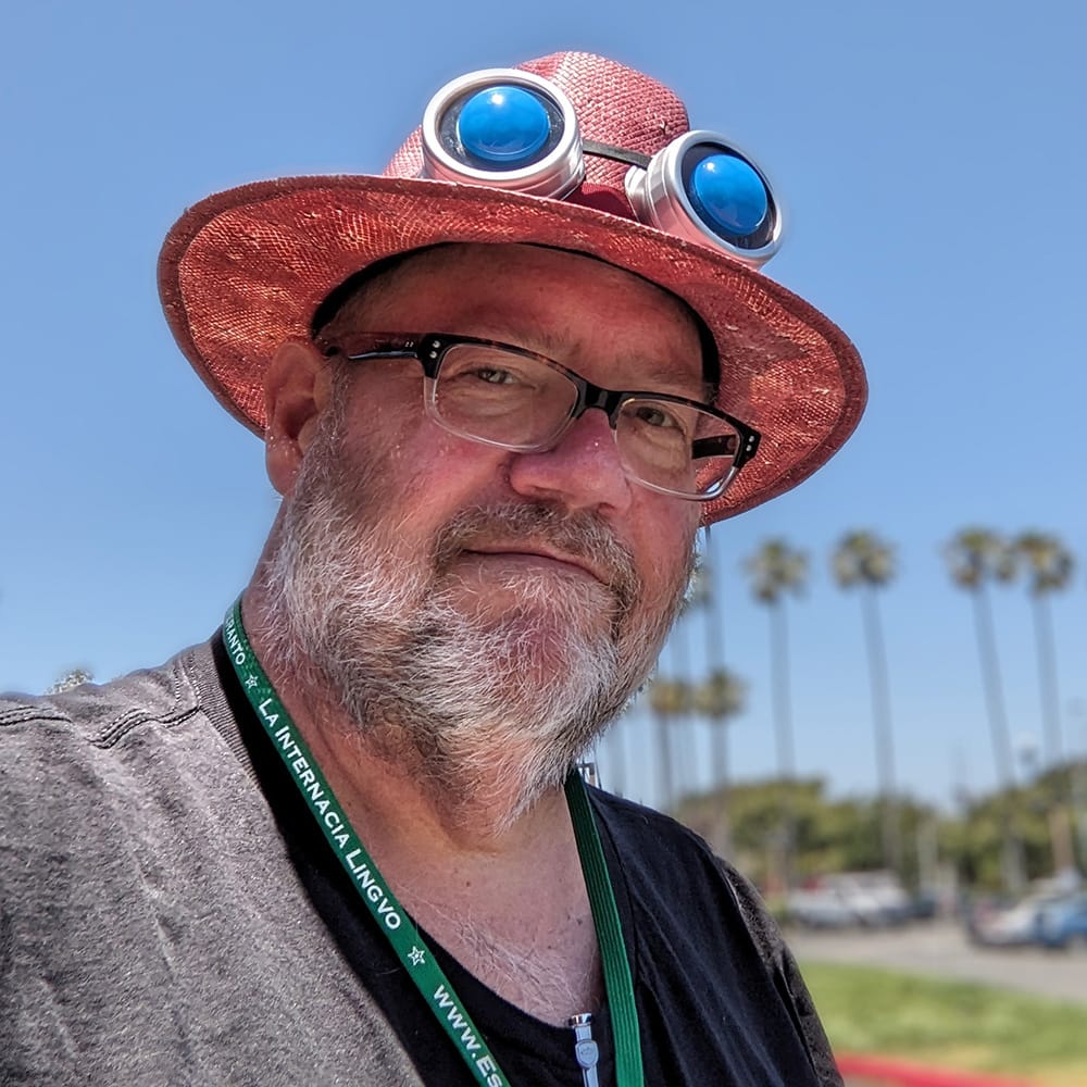 Bearded man in a red sun hat wearing glasses and steampunk glasses over the brim