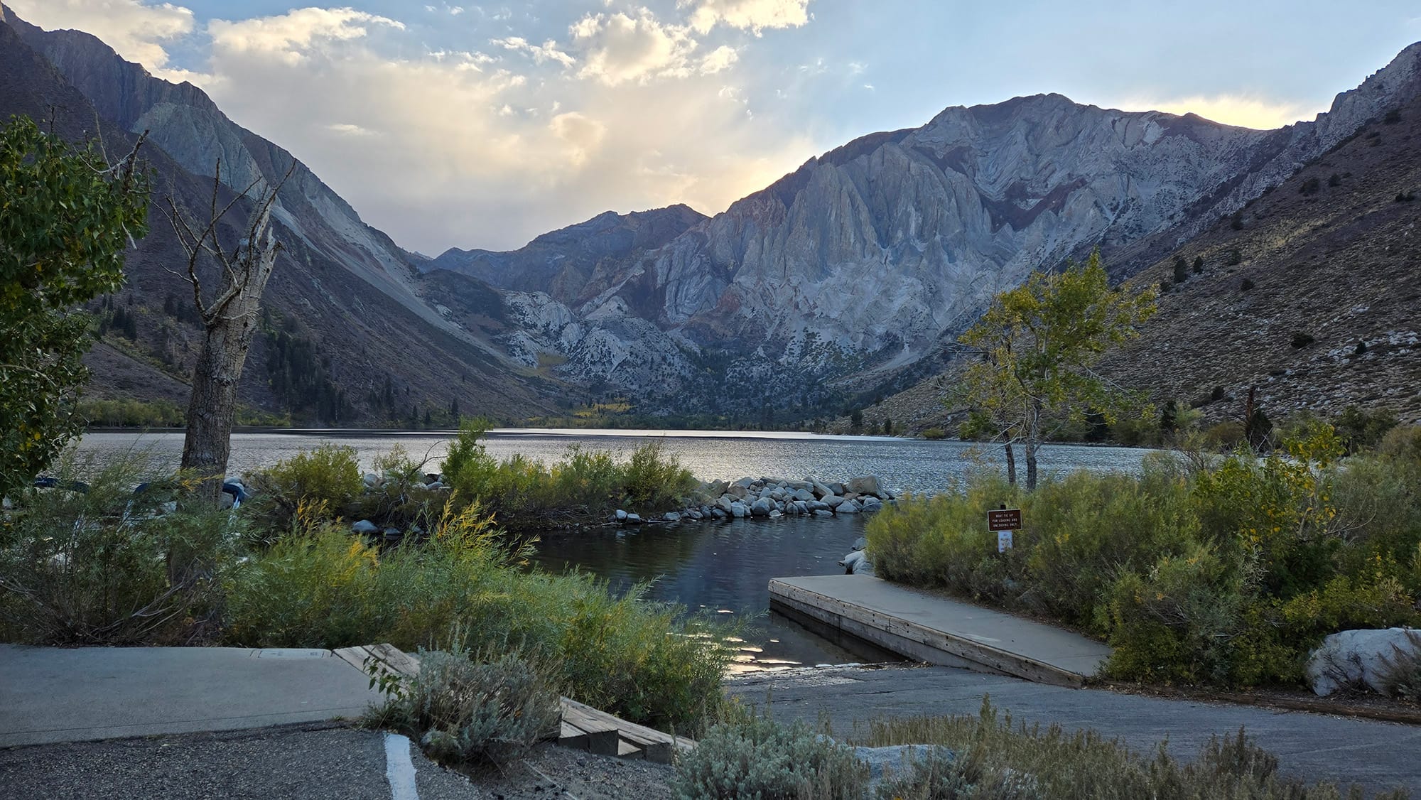 Concrete ramp leading to a small lake. Staggering mountains, clouds, the sun hiding behind