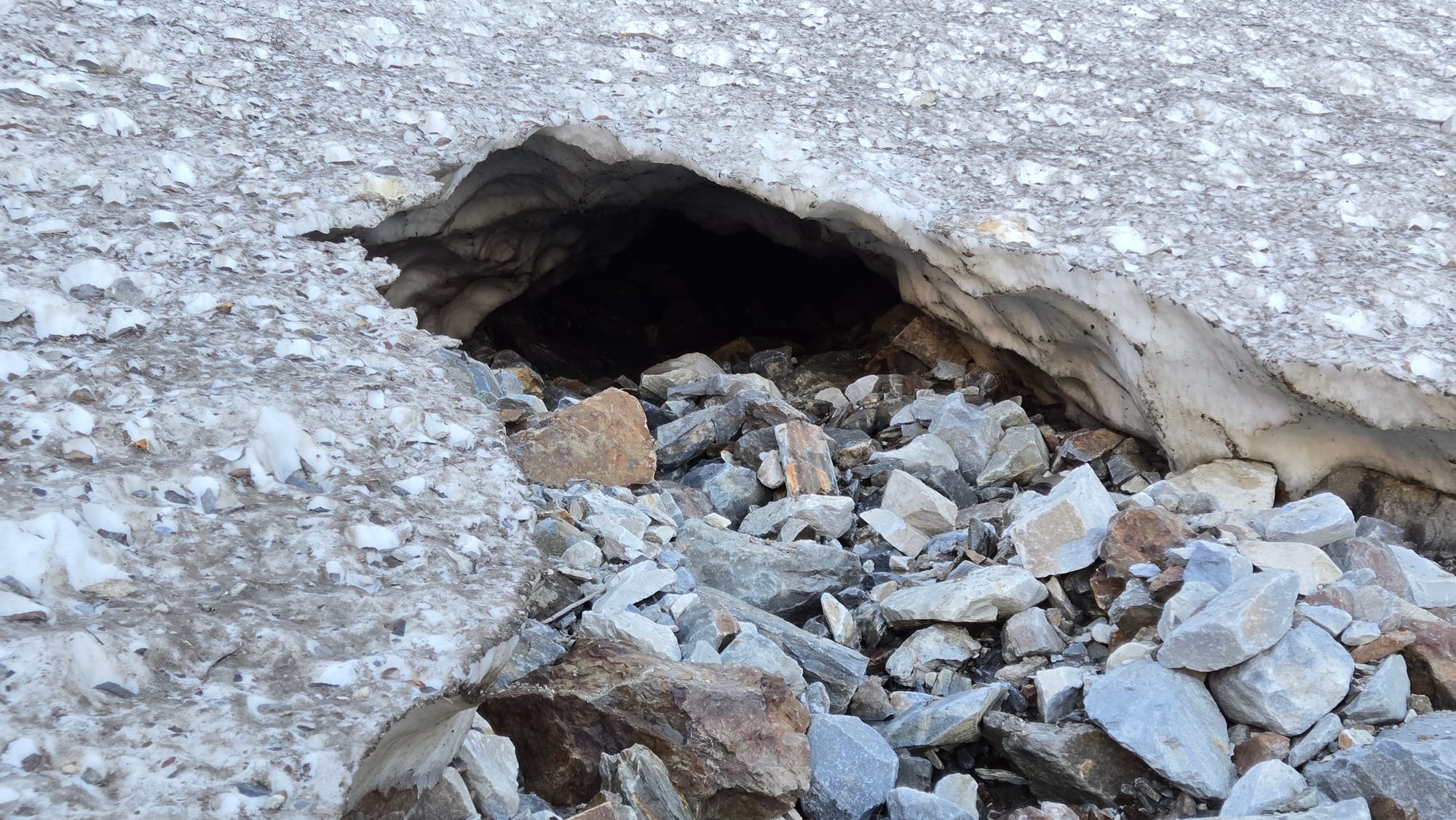 Dirt snow on top of loose rocks. Gaping black hole / ice cave.