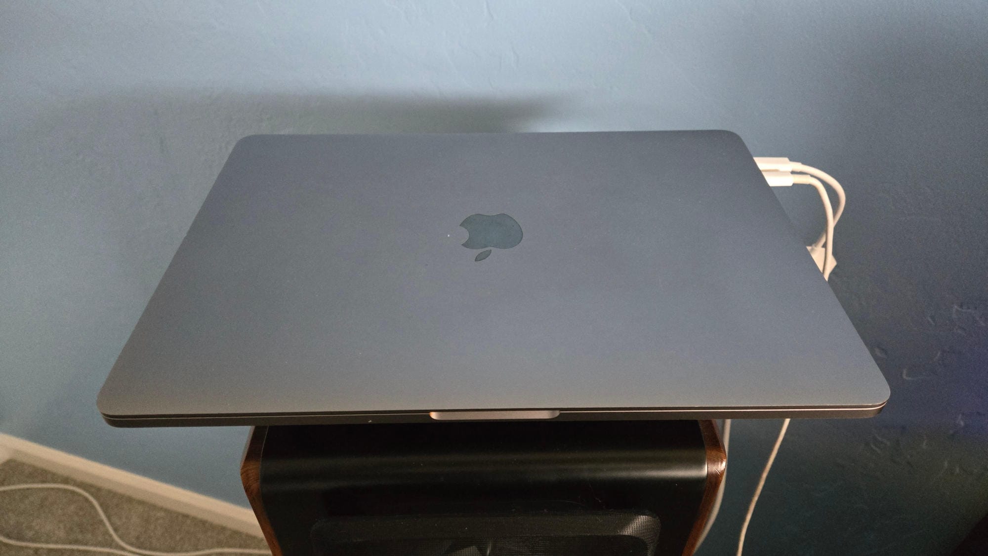 Silver MacBook Pro with two white cords sitting on a speaker