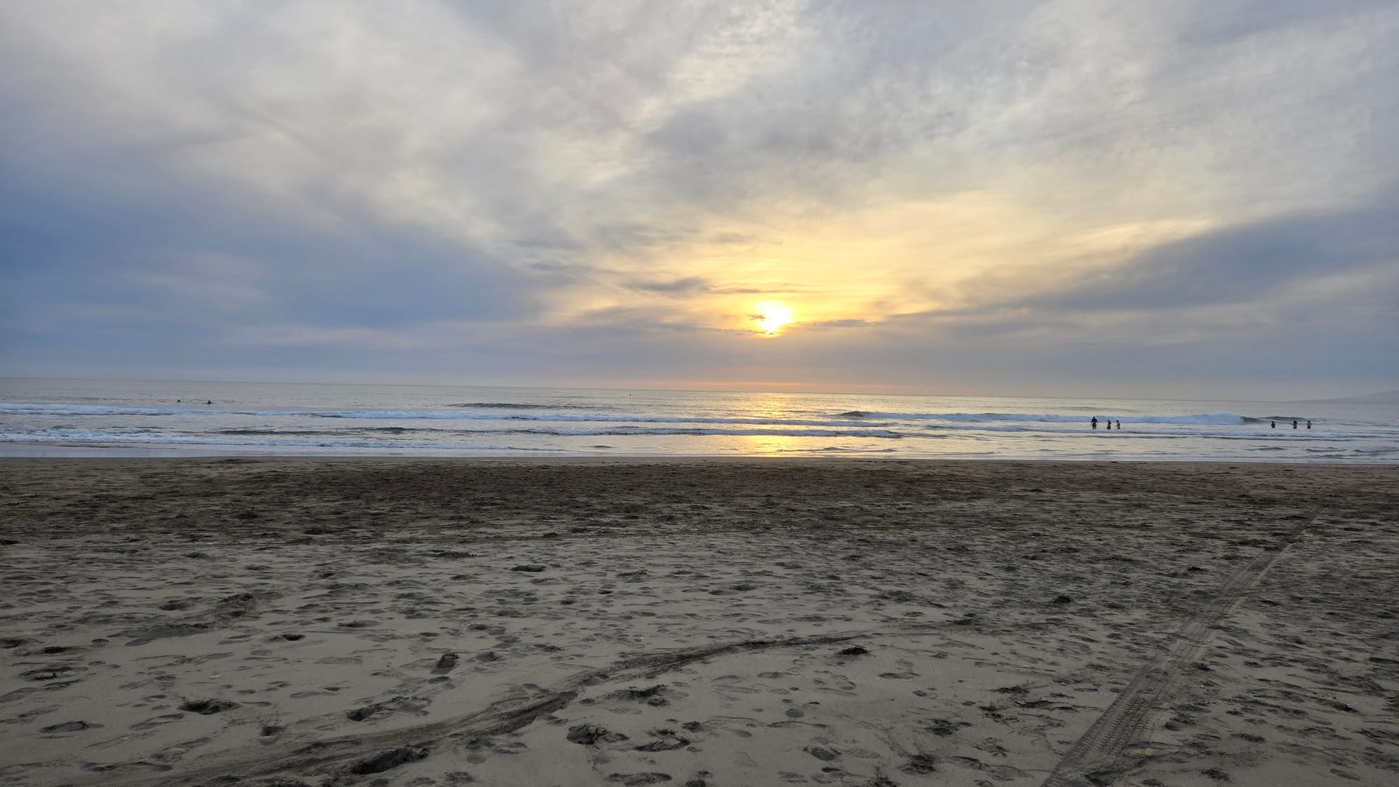 Bright sunset through partial clouds over a sandy beach.