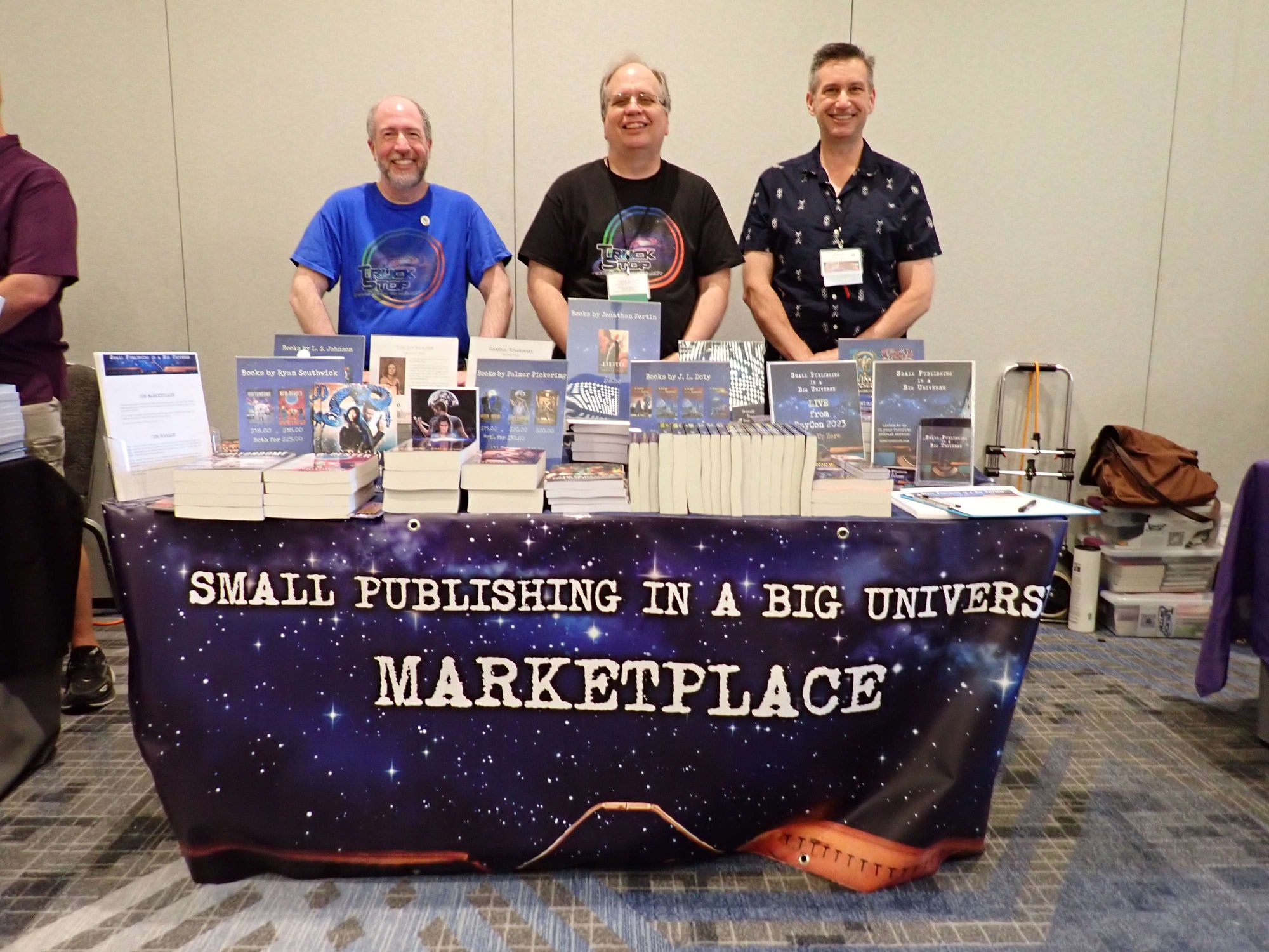3 authors standing behind a table of books: "Small Publishing in a Big Universe Marketplace"
