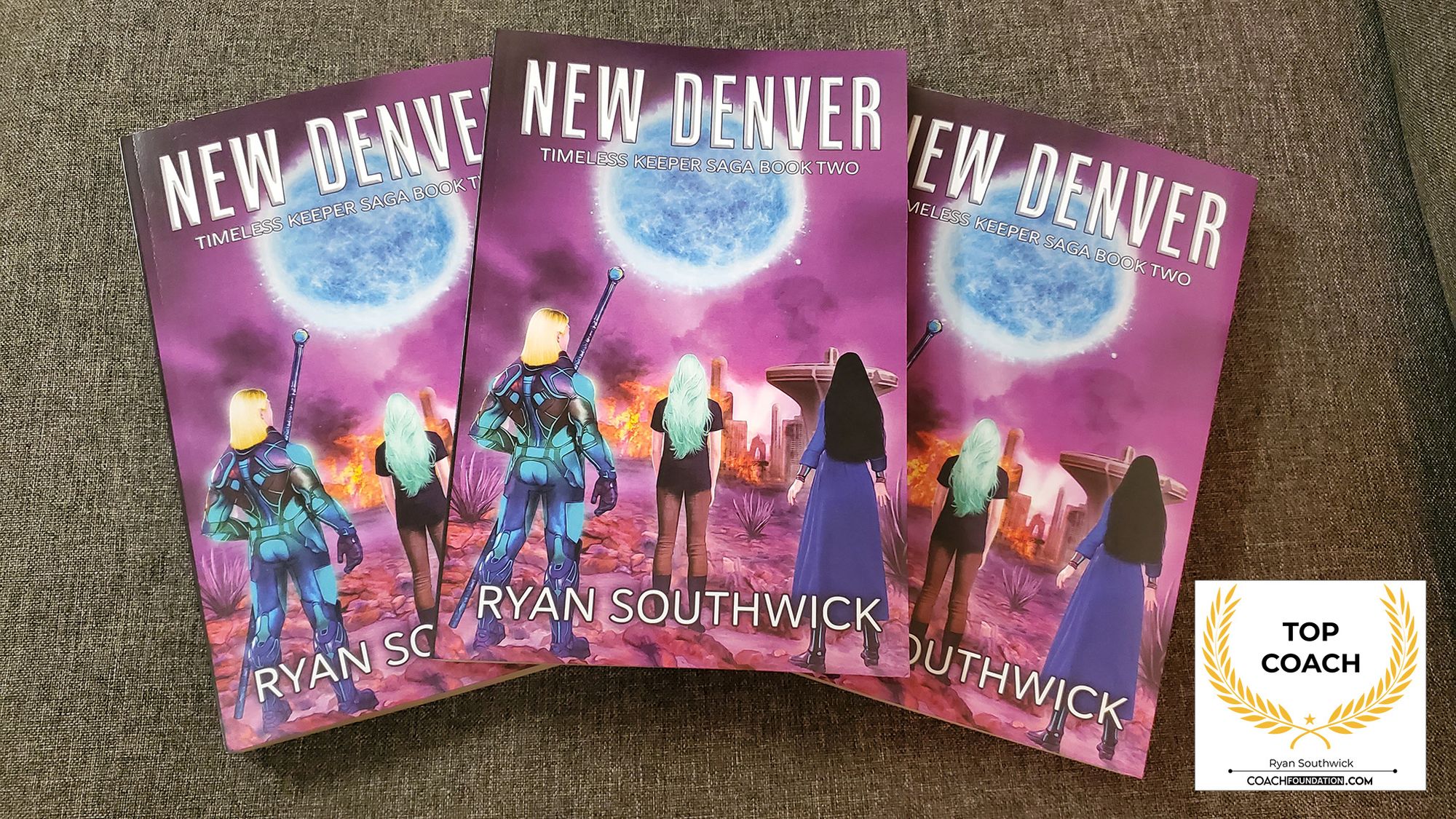 3 paperback copies of New Denver on a material background. "Top Coach" award symbol.