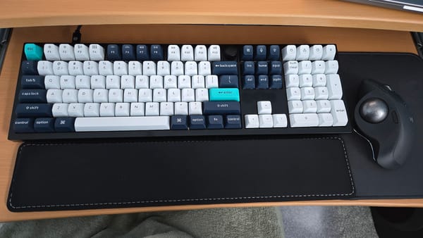 Keyboard with blue and white keys on a tray. Black wrist rest, trackball mouse.